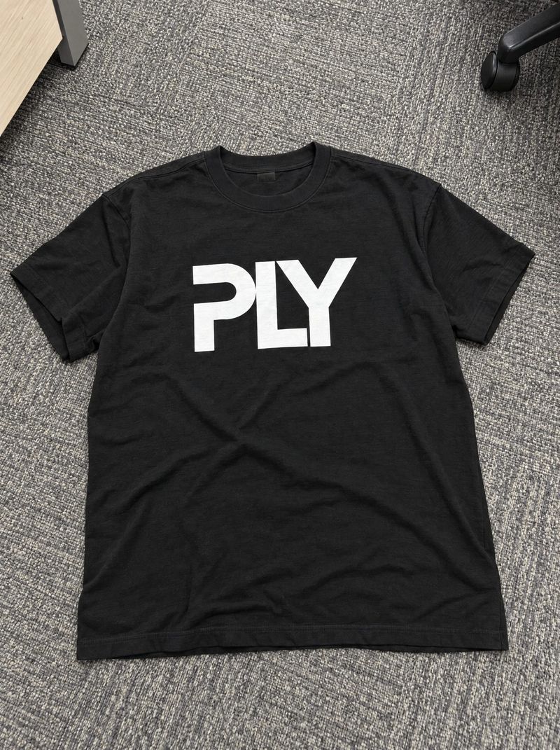 Handyfoto: schwarzes PLY-T-Shirt liegt auf grauem Büroteppich